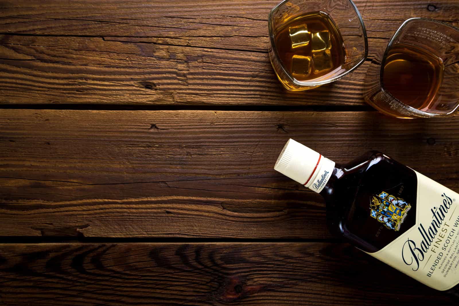 A whiskey glass with ice on dark wood